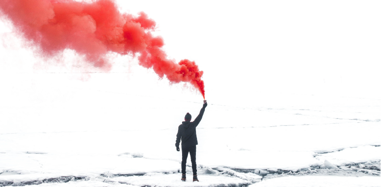 man-on-snowy-landscape-holding-flaree-red-smoke